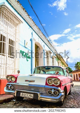 TRINIDAD, CUBA - DECEMBER 8, 2013: Purple and white classic American car and blue colonial building in streets of Trinidad, where old cars are relic of Cuban revolution and still attracts tourists.