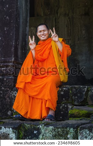 CAMBODIA, SIEM REAP ANGKOR WAT - NOVEMBER 6, 2014: Buddhist monk in reddish yellow robes poses for a photo in one of the famous temples of Angkor Wat, Siem Reap, Cambodia