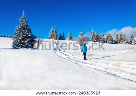Young woman on a mountain trail on a background of a winter landscape with blue sky