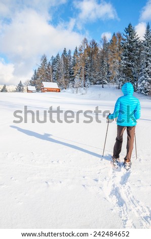 Young woman walking with snow shoes on fresh snow in towards wooden hut in winter landscape