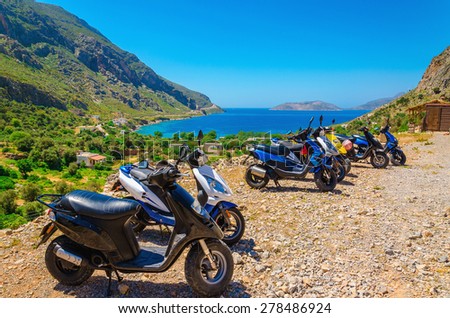 Scooters parked on parking with sea bay with beach behind, Greece
