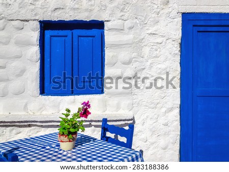 Iconic blue table with wooden chairs and window in front of Greek house, Greece