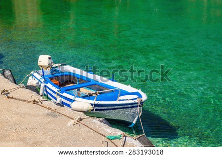 Small open deck motor boat in color of Greek flag moored in cosyport with clear water, Greek Island, southern Greece
