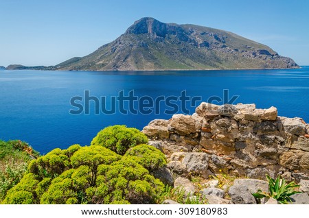 Remote volcanic Island seen from Greek Island Kalymnos with green bushes and clear blue sky, Greece