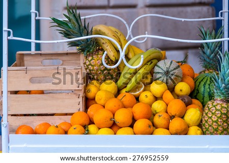 Cart with boxes of oranges, lemons, melons, watermelon, pineapple and bananas against a wall in Syracuse, Sicily, Italy