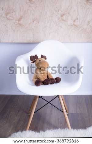 light brown soft toy deer sitting on a white plastic chair that stands on the floor in the  center of the room near the wall