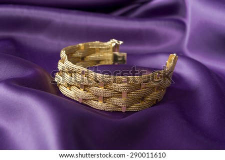 Gold bracelet isolated on purple satin background.