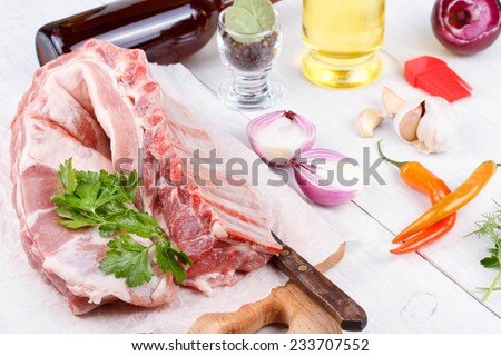 Fresh pork ribs, meat prepared for roast with garlic, parsley, onion and red chili pepper on wooden background