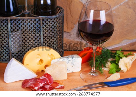 Glass and bottle of wine, cheese and prosciutto, old wooden barrel
