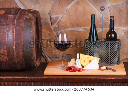Glass and bottle of wine, cheese and prosciutto, old wooden barrel