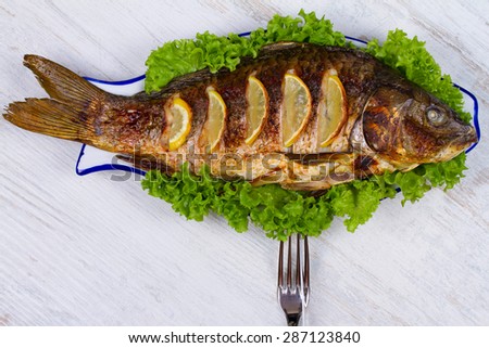 Whole grilled fish carp served with salad and lemon; glass of wine