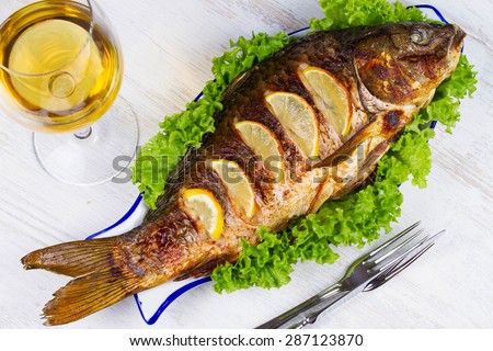 Whole grilled fish carp served with salad and lemon; glass of wine