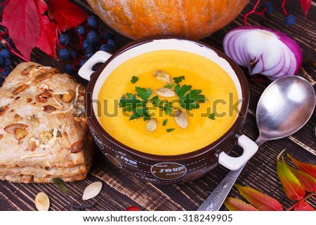 Bowl of pumpkin soup,  whole pumpkin, smoked chicken, bread and red leaves on autumn background