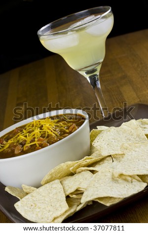 A bowl of chili, with a side of tortilla chips and a margarita