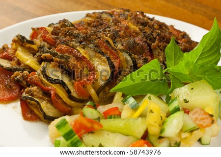 A baked meat and vegetable dish with a side salad of vegetables