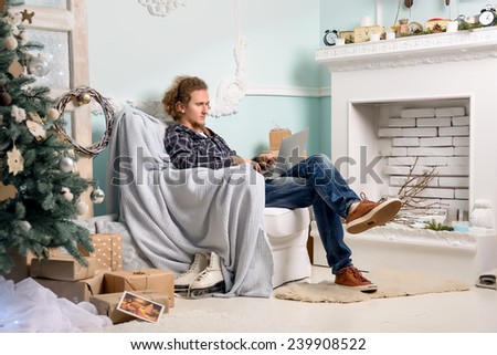 a man sitting in a chair in a Christmas interior, near the fireplace, Christmas tree, looking at laptop, ischit presents, works