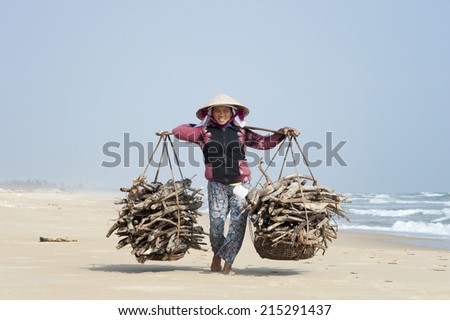 HOI AN - VIETNAM - JANUARY 10, 2014 Old woman carrying heavy bags with wood at the beach in Hoi An, Vietnam. She collects the stranded woods from the sea to sell it at the market.