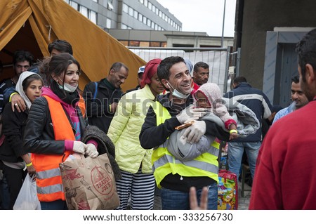 Munich, Germany -September 7th, 2015: A group of Syrian refugees with a small baby are very happy to get to Europe. Civil helpers supply the incoming refugees with warm clothes and blankets.