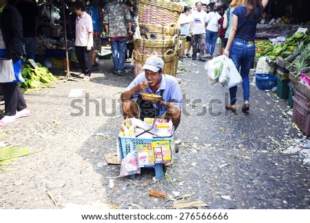 BANGKOK, THAILAND- FEBRUARY 17, 2015: Khlong Toei food market. Local Thai man sitting in the middle of the walking path in the market and eating his lunch. Other people around him continue shopping.