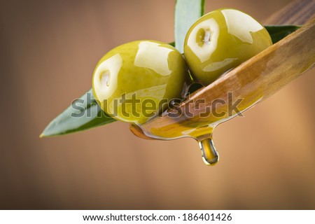 Two olives and leaves with drop oil on wood spoon