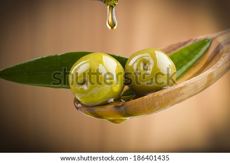 Two olives and leaves with drop oil on wood spoon