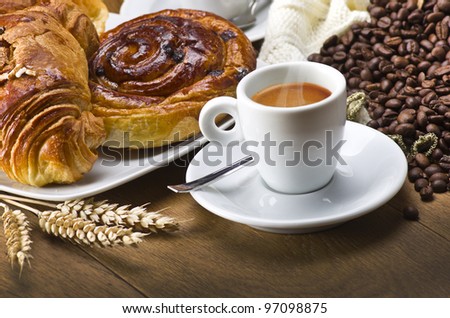 Coffee cup with a croissant and fresh coffee beans on a wood table