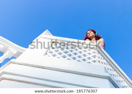 young woman standing on a white balcony and  looking forward