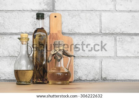 Still life with three bottles of extra virgin healthy Olive oil jug and wooden cutting board on grey bricks background with copyspace