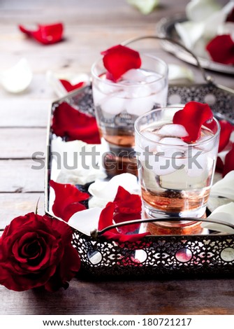 Rose flavor cocktail with ice cubes in glasses with rose flower petals and rose flower bud on a vintage tray