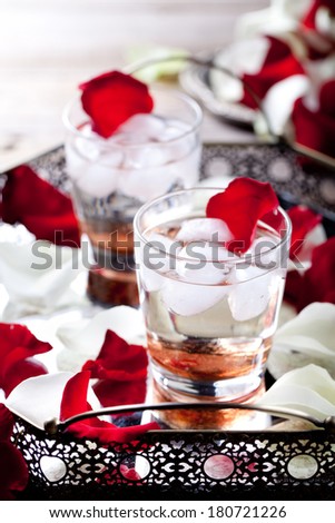 Rose flavor cocktail with ice cubes in glasses with rose flower petals  on a vintage tray