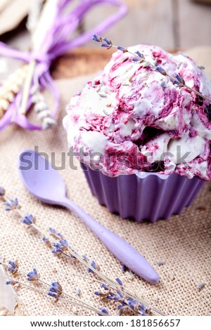 Blackcurrant and lavender ice cream with a lavender flower decoration in a ceramic bowl  on a textile and wooden background. Provence style.