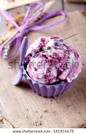 Blackcurrant and lavender ice cream with a lavender flower decoration in a ceramic bowl  on a textile and wooden background. Provence style.