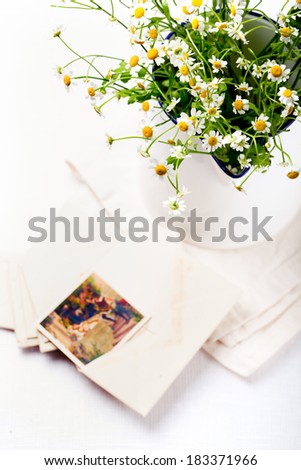 Bunch of chamomile, daisy flowers in an enamel metal vintage jug with a vintage postcards and envelopes on a white textile background