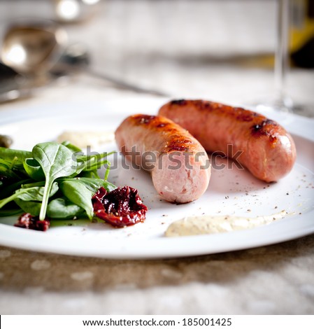 Sausages roasted on a grill with spinach and sun dried tomatoes salad on a white plate on served table background