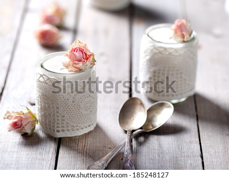 Rose flavor greek yogurt in a glass jar decorated with lace on a wooden background