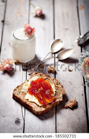 Piece of bread with butter and orange jam and rose flavor yogurt on a wooden table