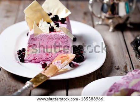 Berry ice cream and white chocolate terrine with white chocolate decor on a white plate on a wooden background