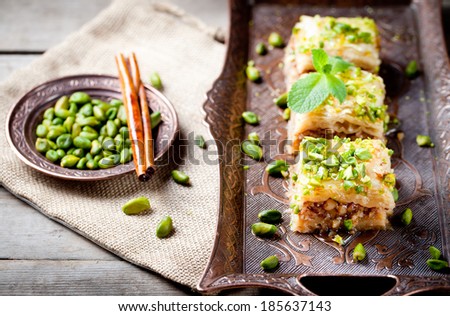 Turkish pistachio and phyllo pastry dessert, baklava on a authentic cooper tray with a plate of pistachios and stick of cinnamon - stock photo