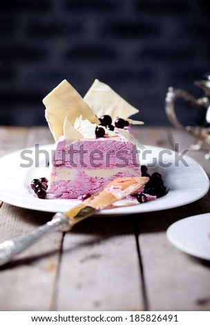 Terrine with berry ice cream in a white chocolate with white chocolate decor on a white plate on a wooden background