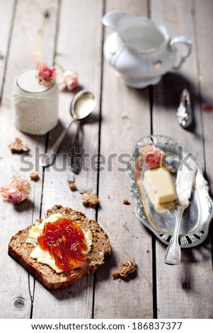 Piece of bread with butter and orange jam and rose flavor yogurt on a wooden table