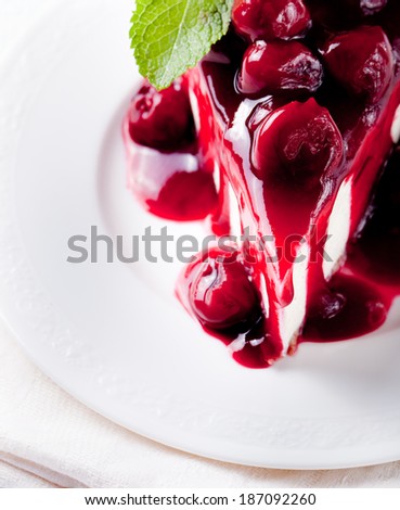 Cheesecake piece with cherry topping sauce and berries on a white plate