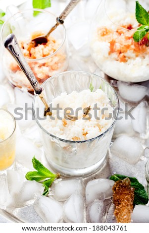 Milk and cardamon, lemon and black tea granita in glasses on a vintage metal tray with ice cubes with fresh mint leaves