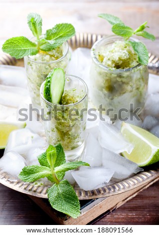 Mint,l lime and fresh cucumber granita in glasses with fresh mint leaves and cucumber slices on a metal tray with ice cubes