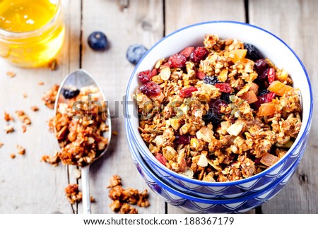 Honey glazed oatmeal, nut and flax seeds granola in a ceramic bowl with honey and fresh berries on a wooden background - stock photo
