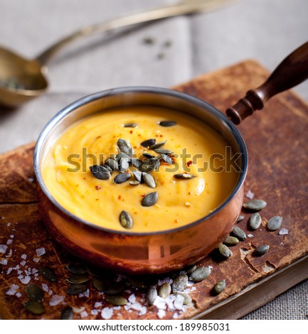 Pumpkin cream soup with pumpkin seeds in a vintage cooper roasting pan on a vintage book and textile canvas background