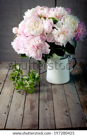 Bunch of peony flowers with green leaves in an enamel jar on a wooden background