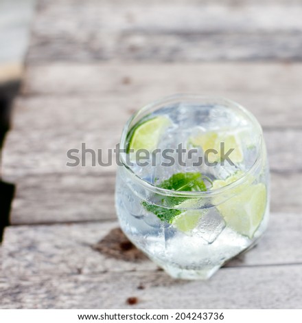 Gin tonic in glass with ice and lime slice on a wooden background. Selective focus.