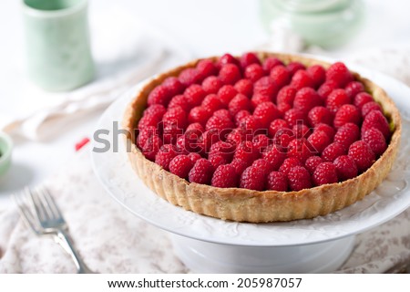 Fresh raspberry and pistachio cream tart on a white textile background.