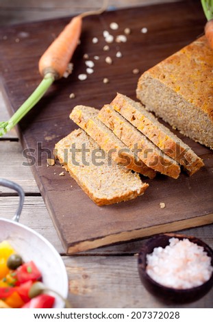 Red and yellow fresh tomato salad with capers, olive oil and carrot and oatmeal bread on a wooden background
