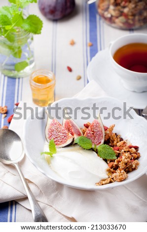 Honey glazed oat, goji berries granola with fresh figs and yogurt with a cup of tea on a textile blue and white background
